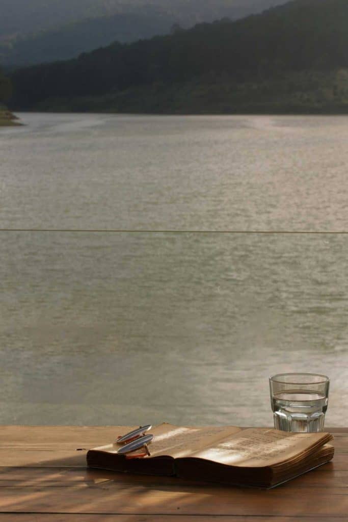 glass of water and open book on a table with lake in the bakcground